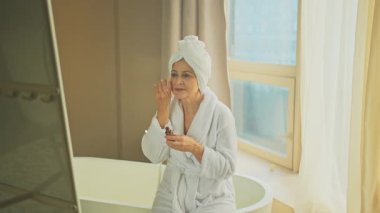 Cilde doğal damla kozmetik yağı süren bir kadın. Yetişkin yaşlı bir kadın günlük güzellik rutini yapan pipetli anti-yaş serumu uyguluyor. Yaşlı kadın yüz bakımı yaptırıyor.