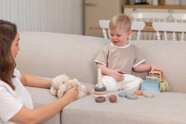 Evde mutlu bir aile. Anne ve bebek evdeki kanepede oyuncaklarla oynuyor. Küçük çocuk ve bebek bakıcısı birlikte eğleniyorlar. Genç kadın, anne, çocuk oturma odasında dinleniyor.