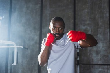 Beden eğitiminde. Afrikalı dövüşçü boksörlere yumruk atmaya hazır koruyucu bandajları kameraya sarar. Güçlü bir adam boks antrenmanına hazırlanıyor.