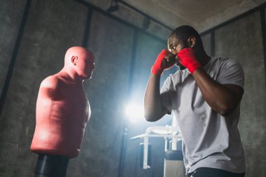 Beden eğitiminde spor. Güçlü bir Afrikalı dövüşçü kum torbasıyla yumruk atma eğitimi alıyor. Kickboksör boksör kuklayı yumrukluyor. Spor salonunda eğitim günü. Dövüş sanatları kickboks dövüşü