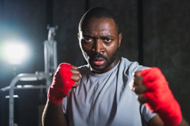 Spor salonunda boksör. Saldırgan Afrikalı dövüşçü boks eğitiminden sonra dinleniyor kameraya bakarak dövüşmeye hazır. Güçlü terli adam yumruklarını eğitiyor. Doğruca antrenmana hazırlanıyor.