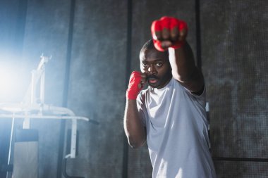 Beden eğitiminde. Afrikalı dövüşçü boksörlere yumruk atmaya hazır koruyucu bandajları kameraya sarar. Güçlü bir adam boks antrenmanına hazırlanıyor.