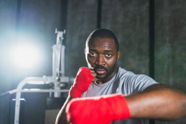 Beden eğitiminde. Afrikalı dövüşçü boksörlere yumruk atmaya hazır koruyucu bandajları kameraya sarar. Güçlü bir adam boks antrenmanına hazırlanıyor.