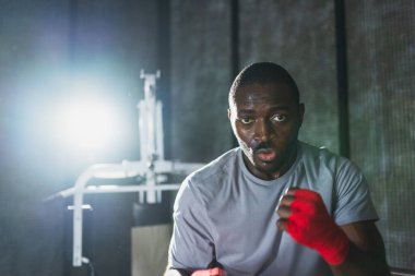 Beden eğitiminde. Afrikalı dövüşçü boksörlere yumruk atmaya hazır koruyucu bandajları kameraya sarar. Güçlü bir adam boks antrenmanına hazırlanıyor.