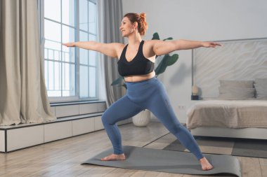 Yoga fitness antrenmanı. Evde yoga yapan bir kadın. Artı ev içinde yoga minderiyle spor egzersizi yapan beden bir kadın. Spor giyim bölümündeki kız kilo vermek için antrenman yapıyor. Spor ve zindelik