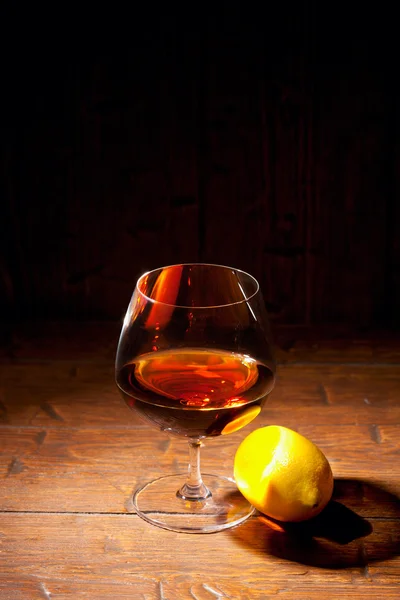 Glass of cognac with lemon on wooden background — Stock Photo, Image