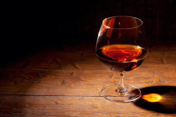 Glass of cognac with lemon on wooden background — Stock Photo, Image