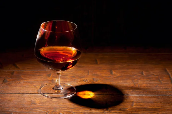 Glass of cognac with lemon on wooden background — Stock Photo, Image