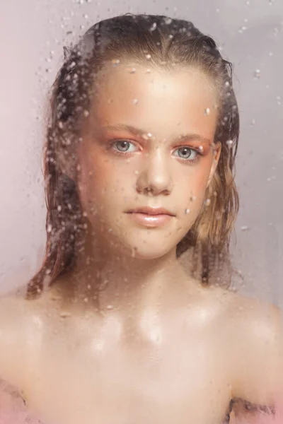 Mulher bonita nova com pele perfeita atrás de um copo com gotas de chuva em fundo rosa — Fotografia de Stock