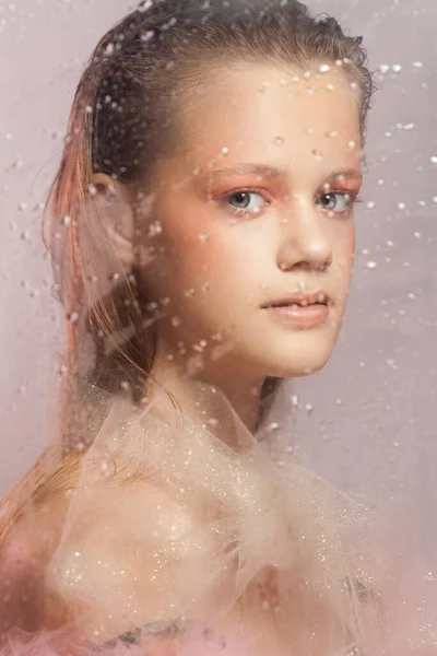 年轻美丽的女人，完美的皮肤和粉色背景的雨滴在玻璃杯后面 — 图库照片