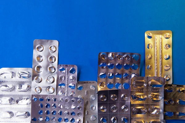 Empty blister packs of pills in the form city on blue background. — Stock Photo, Image