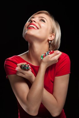 Güzel sarışın kadın gülümsüyor ve siyah arka planda kumar fişleri gösteriyor.