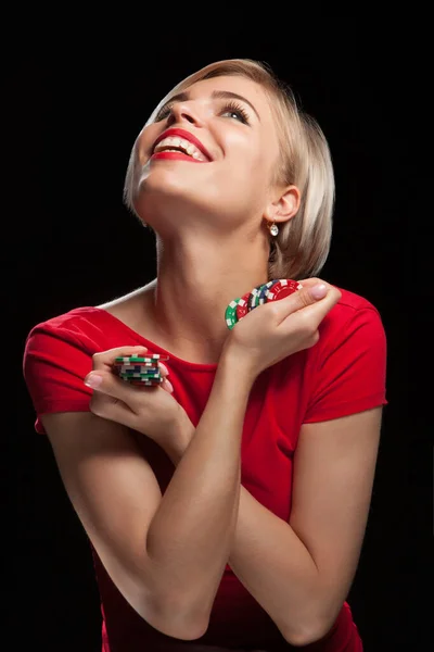 Hermosa mujer rubia sonriendo y mostrando fichas de juego sobre fondo negro —  Fotos de Stock