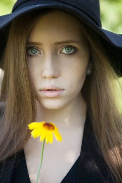 Belle jeune femme dans une robe noire et un chapeau noir à fleur jaune — Photo