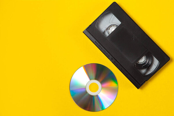 Video cassette videotape and compact disc on a yellow background. Top view. Save your memories on modern media. Flat lay concept.