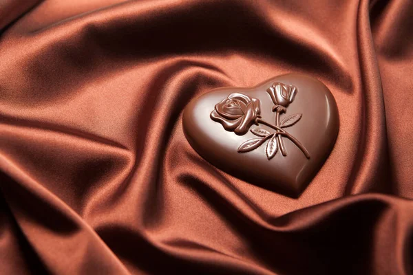 茶色の絹の上に花のパターンを持つハート型のチョコレート. — ストック写真