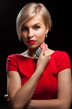 Güzel sarışın kadın siyah arka planda kumar fişleri gösteriyor.