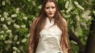 Çiçekli kuş kirazının yanında zıplayan uzun dalgalı saçlı bir kadın. Bahar geldi. Çiçek açan doğa.