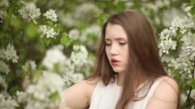 Uzun dalgalı saçlı bir kadın çiçek açan elma ağacının yanında rahatlar.