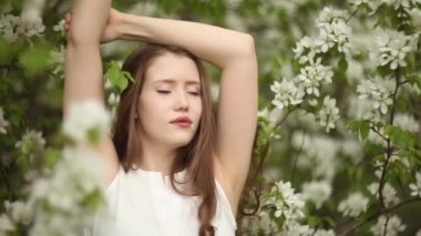 Uzun dalgalı saçlı bir kadın çiçek açan elma ağacının yanında rahatlar.