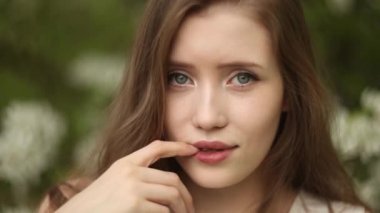 Uzun dalgalı saçlı tatlı utangaç kadın çiçek açan elma ağacının yanında rahatlıyor.