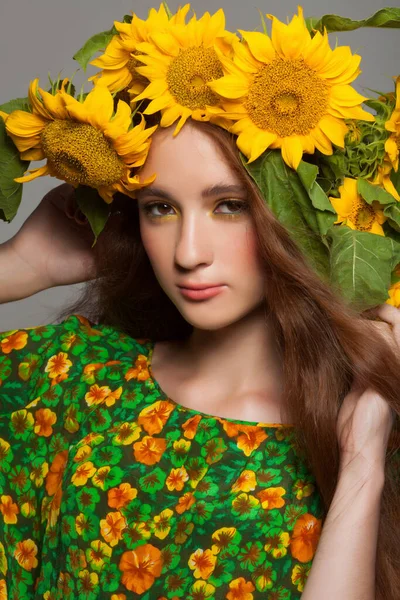 Vrouw met stijlvolle make-up en zonnebloemen rond haar hoofd — Stockfoto