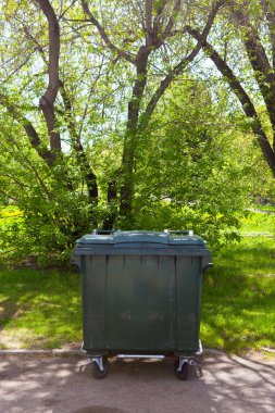 Ağaç arka planının önündeki sokak yakınındaki parktaki çöp bidonları.