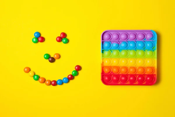 Gökkuşağı silikon duyusal anti-stres oyuncağını sarı arkaplanda renkli şekerlerden gelen gülücüklerle fırlat. — Stok fotoğraf