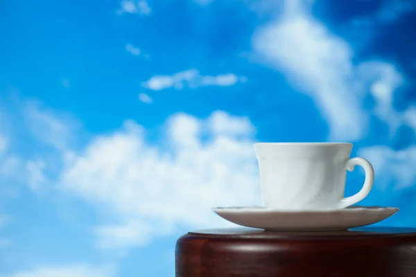 Taza blanca de café o té con vapor sobre una mesa de madera sobre un fondo de cielo azul — Foto de Stock