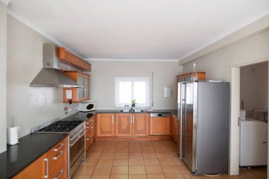 Ahşap dolapları ve granit tezgahı olan büyük ama modası geçmiş bir mutfak.