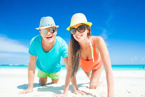 Pareja en ropa brillante y sombreros sentados en la playa tropical de arena —  Fotos de Stock