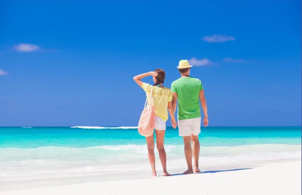 Couple in bright clothes and hats walking at tropical beach — Stock Photo, Image