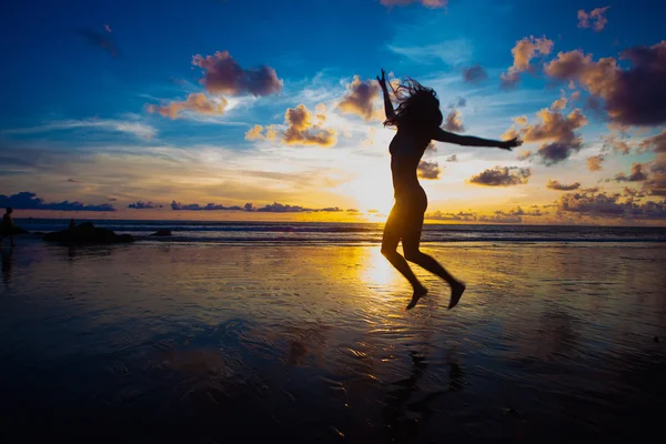 Sunset silhouette of young fit woman jumping at beach — Stock Photo, Image