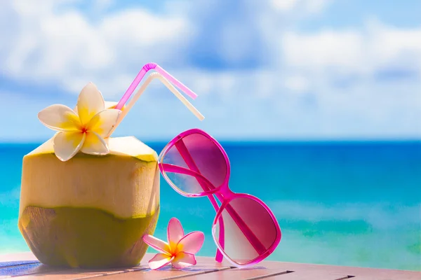 Foto de coquetel de coco fresco e óculos de sol rosa na praia tropical — Fotografia de Stock