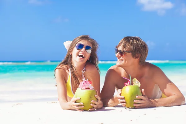 Feliz jovem casal deitado em uma praia tropical em Barbados e beber um coquetel de coco — Fotografia de Stock