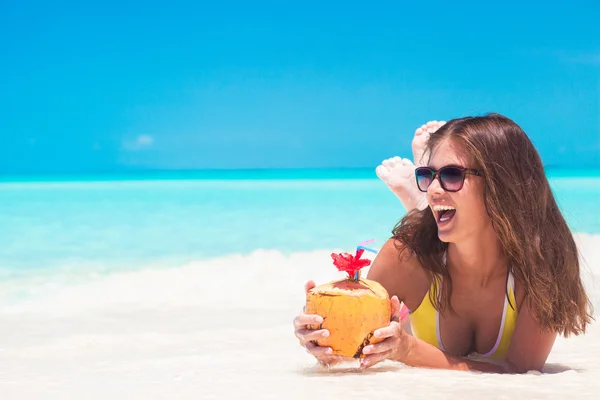 Jonge vrouw die lacht liggen in bikini en zonnebril met kokos op strand — Stockfoto