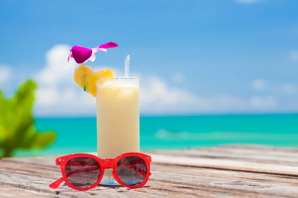 Fresh exotic banana and pineapple cocktail and sunglassses on a wooden table by the beach — Stock Photo, Image