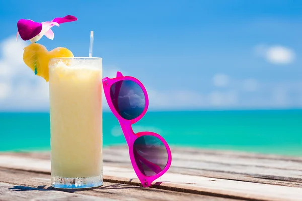 Fresh exotic banana and pineapple cocktail and sunglassses on a wooden table by the beach — Stock Photo, Image