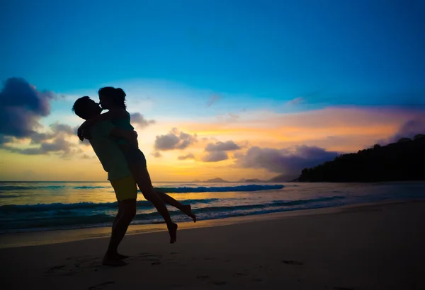 Jong koppel in liefde knuffelen op strand bij zonsondergang — Stockfoto