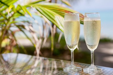 Two glasses of chilled prosecco over tropical background