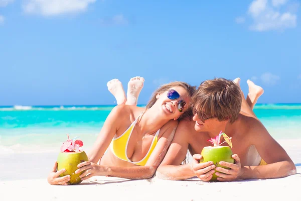 Счастливая молодая пара лежит на тропическом пляже в Барбадосе и пьет кокосовый коктейль — стоковое фото