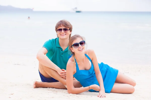 Romantic couple in bright clothes sitting and hugging at a tropical beach — Stock Photo, Image