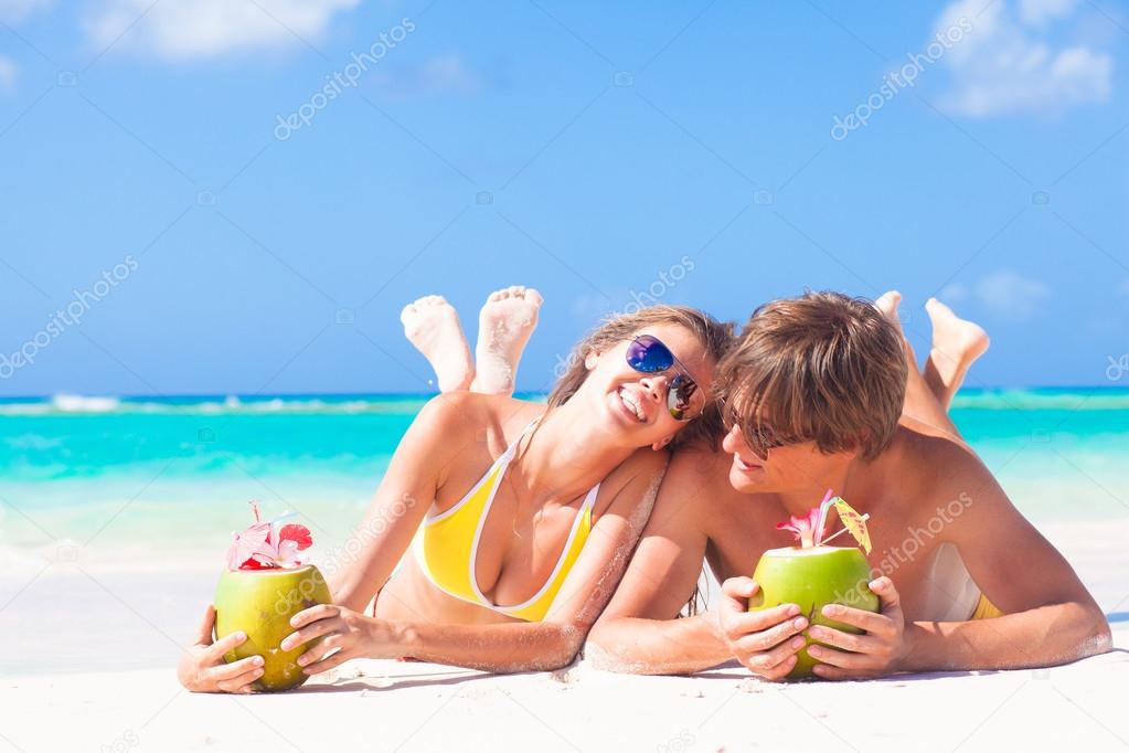 happy young couple lying on a tropical beach in Barbados and drinking a coconut cocktail