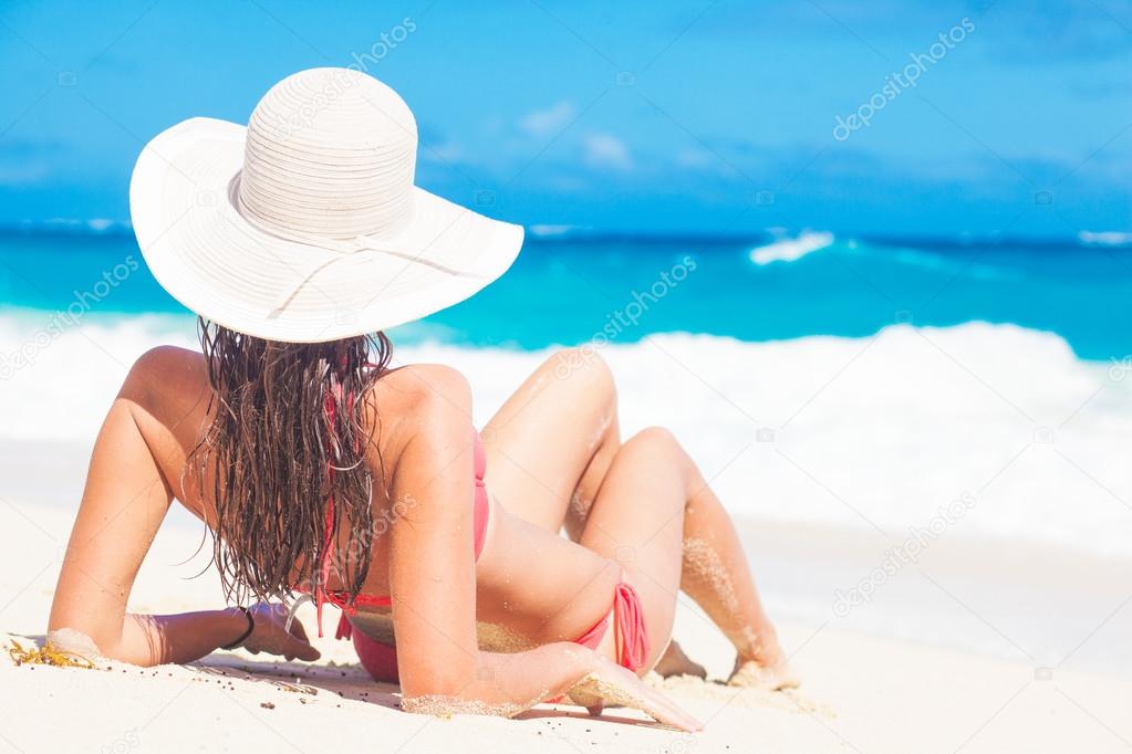 back view of long haired girl in bikini and straw hat on tropical caribbean beach
