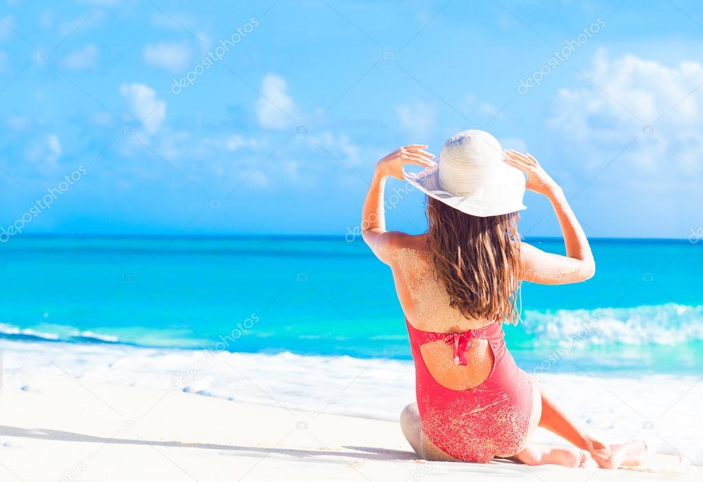 back view of long haired girl in red swimsuit and straw hat on tropical caribbean beach