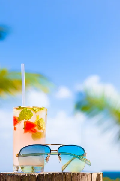 Szklanka schłodzonego mohito koktajl i okulary na stole w pobliżu plaży — Zdjęcie stockowe