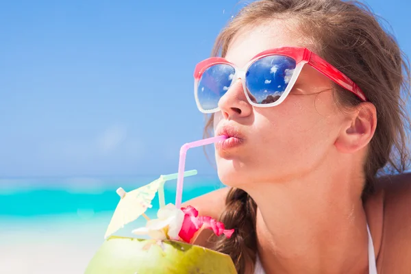 Jovem mulher sorrindo deitado em chapéu de palha em óculos de sol com coco na praia — Fotografia de Stock