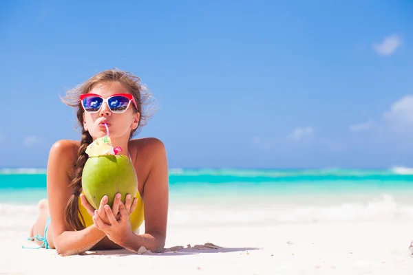 Jovem mulher sorrindo deitado em chapéu de palha em óculos de sol com coco na praia — Fotografia de Stock