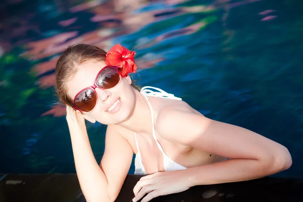 Vacker ung kvinna i solglasögon med blomma i håret leende i lyx pool — Stockfoto