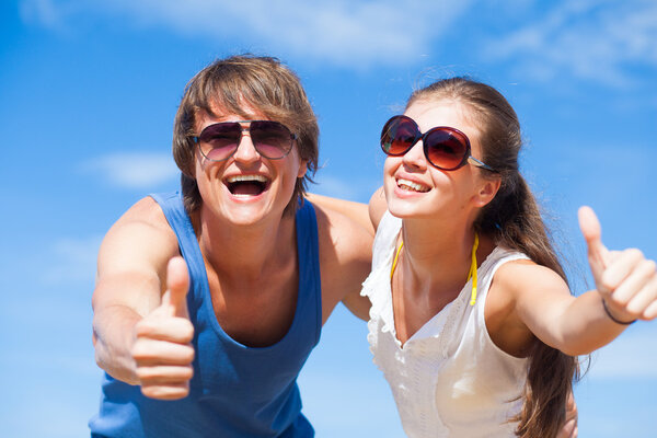 Portrait of happy young couple in sunglasses having fun on tropical beach. Thumbs up